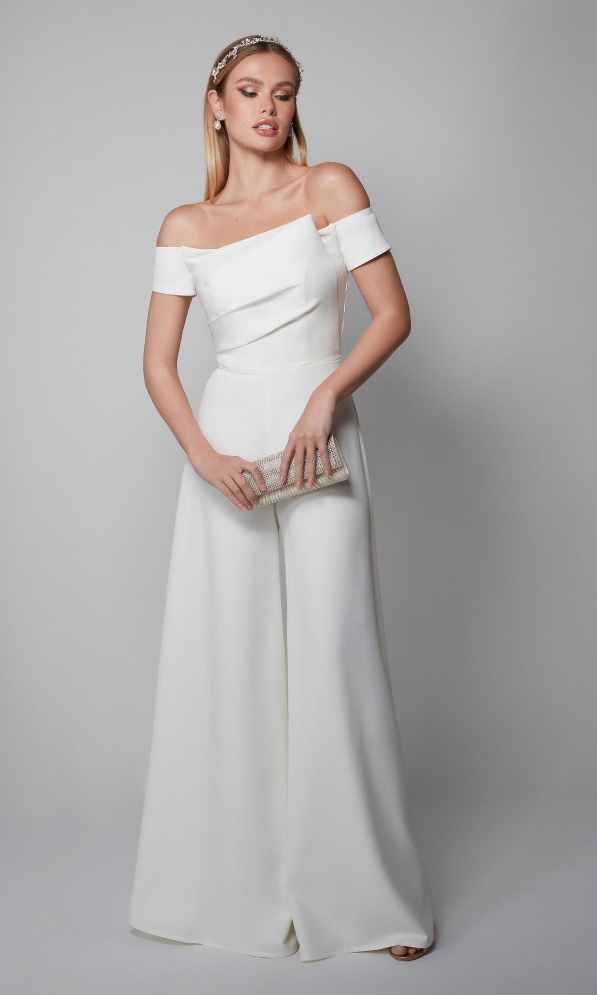 Woman in an ivory Long Formal Jumpsuit: Alyce 70014, holding a silver clutch, stands against a plain light gray background.